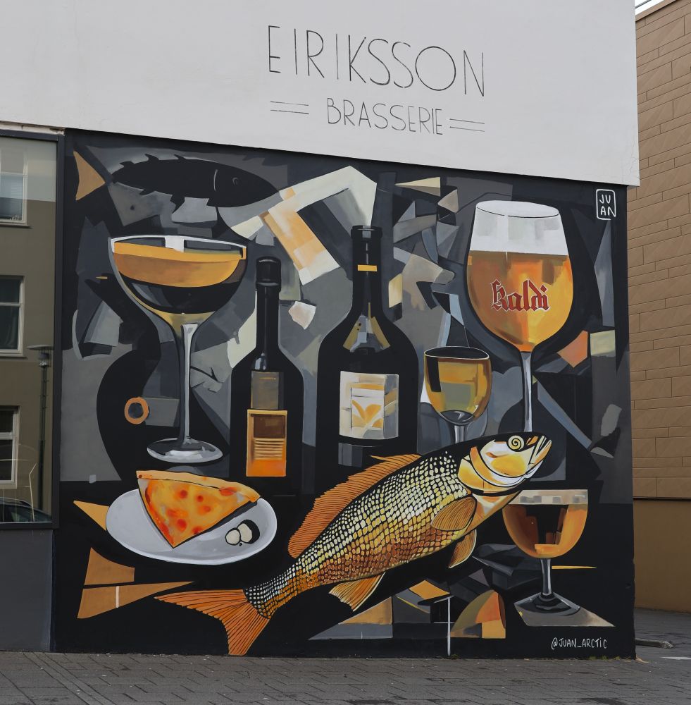 Juan Arctic at Eriksson Brasserie Juan Arctic is a favorite muralist known for his playful and colorful artwork. The author recalls seeing his murals daily while living in Reykjavik and appreciates the context he brings to his work.